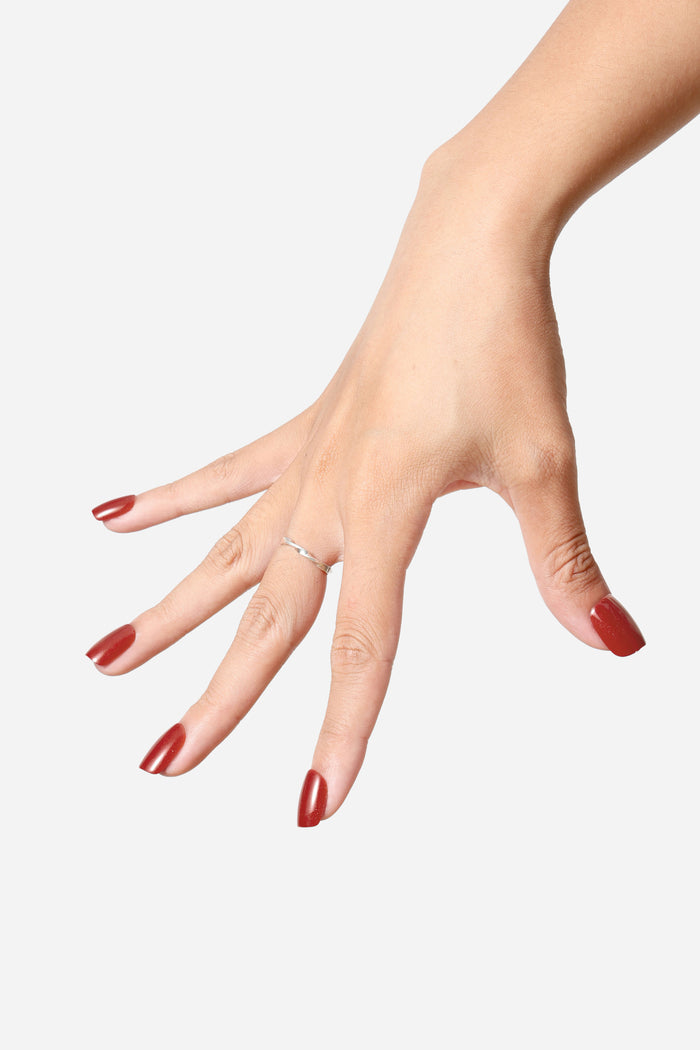 Woman's hand with glossy, wine-red, square press-on nails and a silver ring.