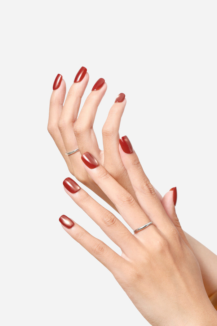 Close-up of hands with glossy, wine-brown, square press-on nails and simple silver rings.