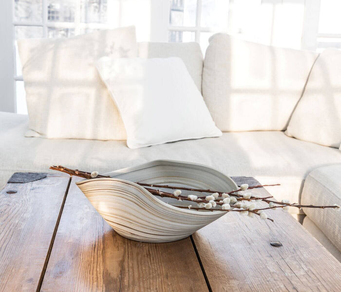 Gray and cream striped ceramic bowl with curved leaf shape, holding dried branches and white berries on wooden table.