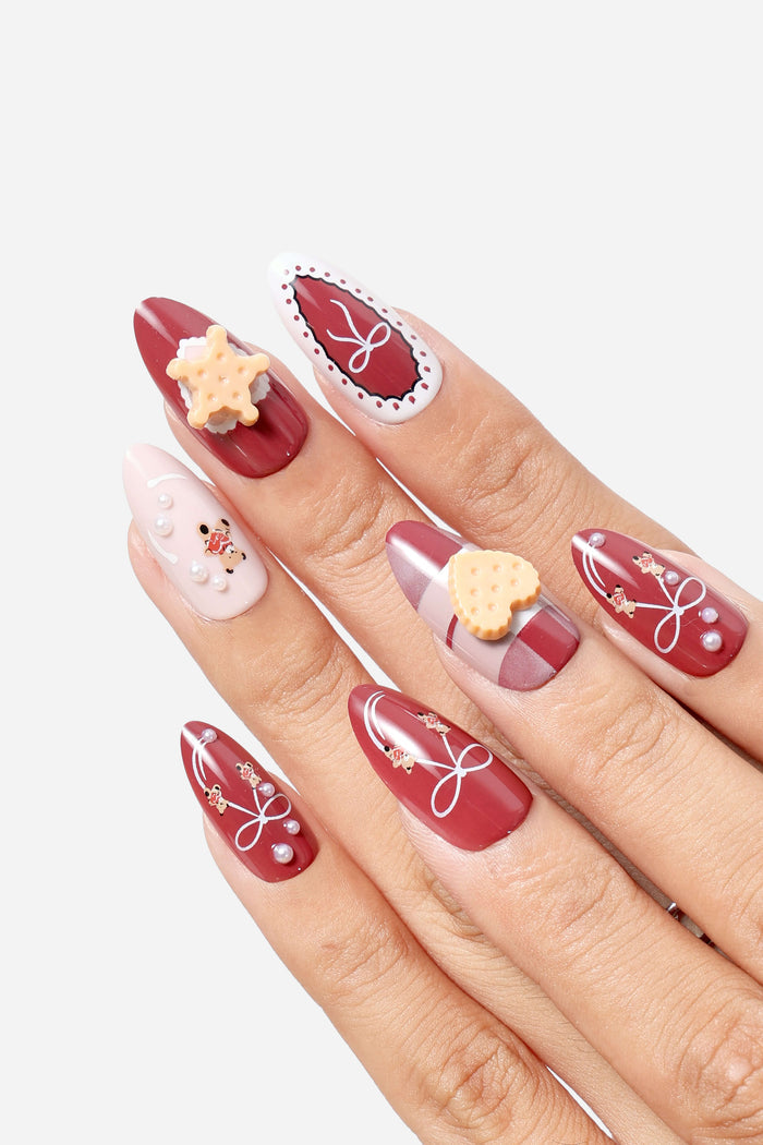 Almond press-on nails with a burgundy base, featuring white bow designs, pearl accents, and cute bear and heart charms.