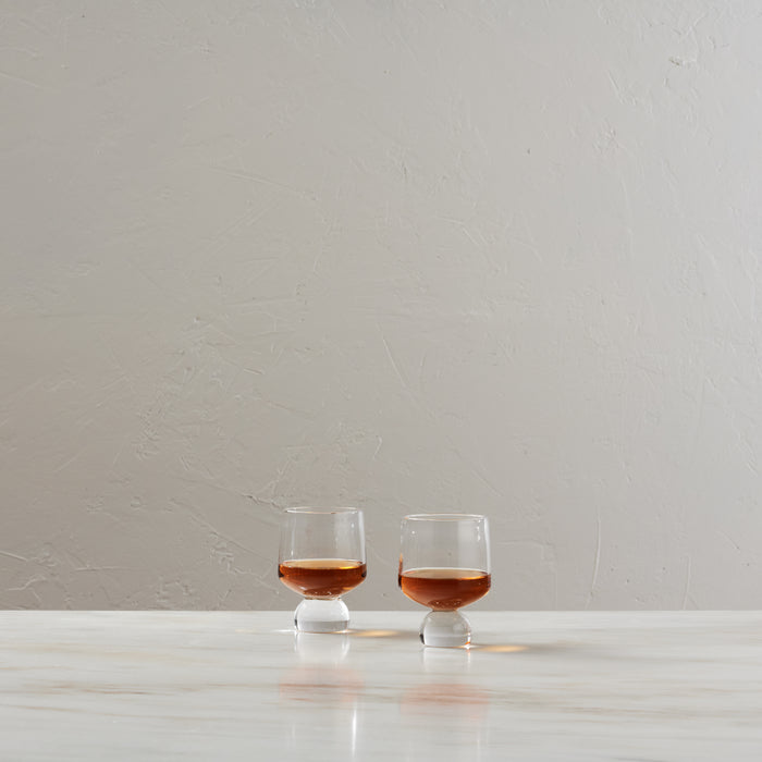 Two glasses filled with bourbon on a white surface against a neutral background.