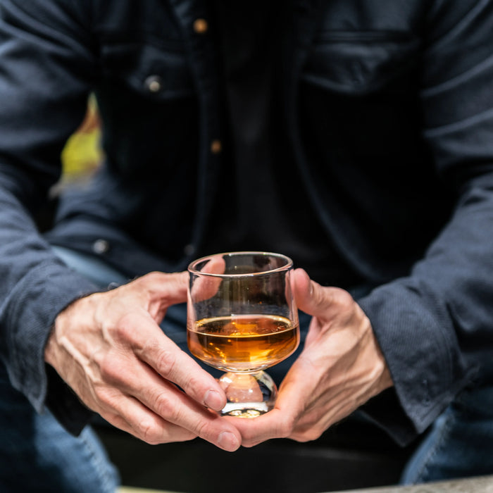 Person in dark jacket holding a glass of amber bourbon.