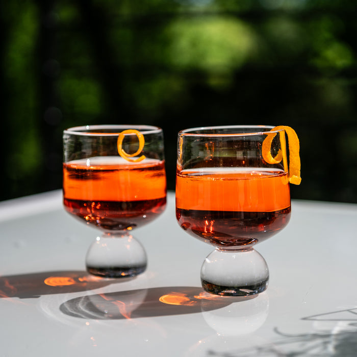 Two glasses filled with amber bourbon and garnished with orange peels on a white surface.