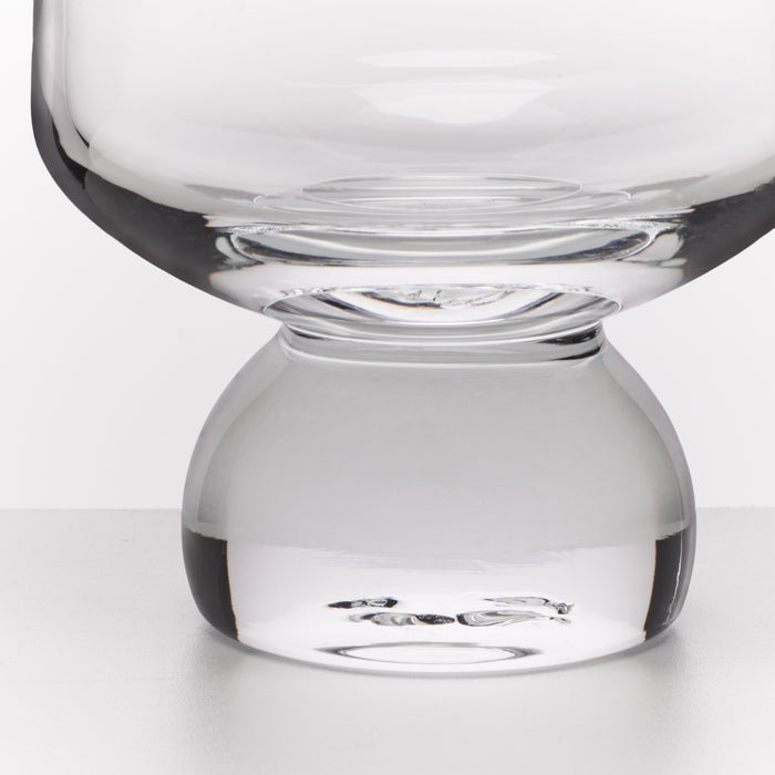 A close-up studio shot of a clear glass vessel with a wide rounded bowl and a thick bulbous base, photographed against a light gray background.