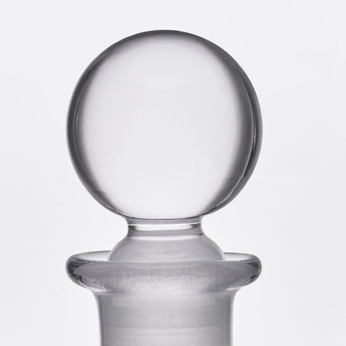 Clear glass decanter with spherical stopper and wide pouring lip on cylindrical neck.