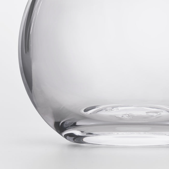 Clear glass decanter with curved body and wide base, shown from a side angle.