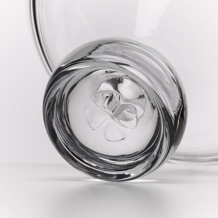 A close-up studio shot of a clear glass tumbler with a thick rim and a sculptural, organic glass base, set against a clean white background.