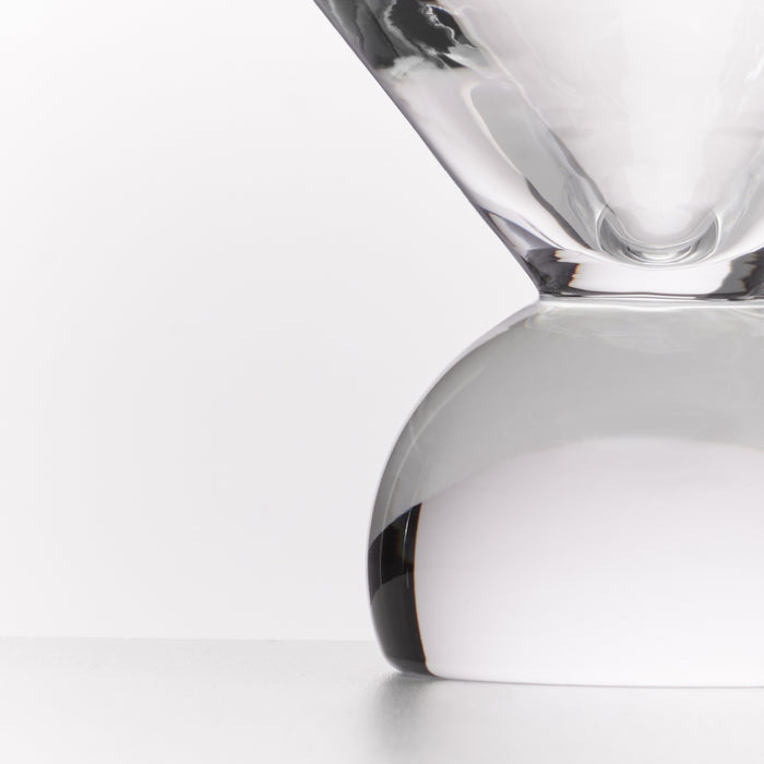 A close-up studio shot of a clear glass hourglass with a smooth rounded base and a narrow top chamber, photographed against a clean white background.