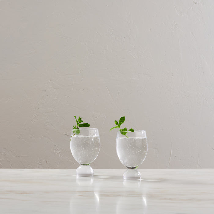 Two clear glass tumblers with white pedestal bases filled with water and garnished with mint sprigs.