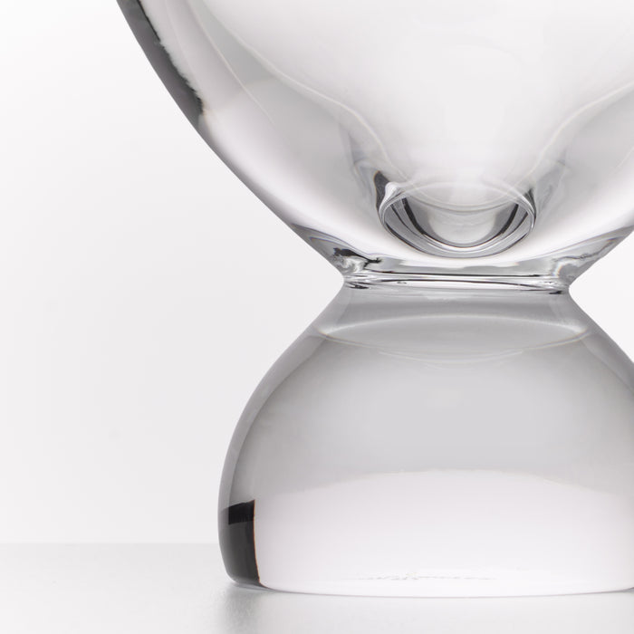 A close-up studio shot of a transparent glass hourglass with a smooth, rounded design on a light gray background.