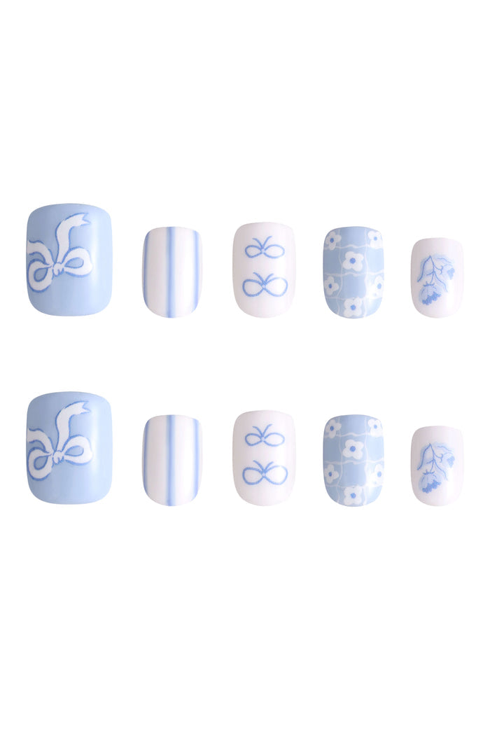 Pastel blue press-on nails with white ribbon, stripes, bows, and floral designs.