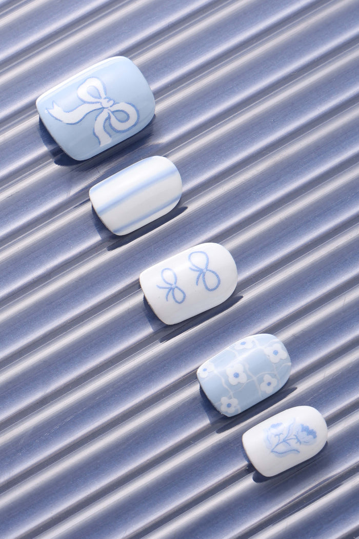 Blue Belle press-on nails with bow, stripe, double bow, floral, and single flower designs.
