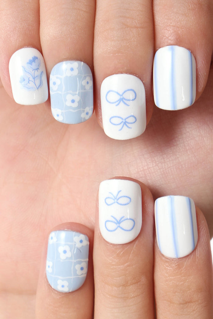 Blue Belle by Elaine Lee press-on nails featuring floral, bow, and stripe designs on white and pastel blue backgrounds.