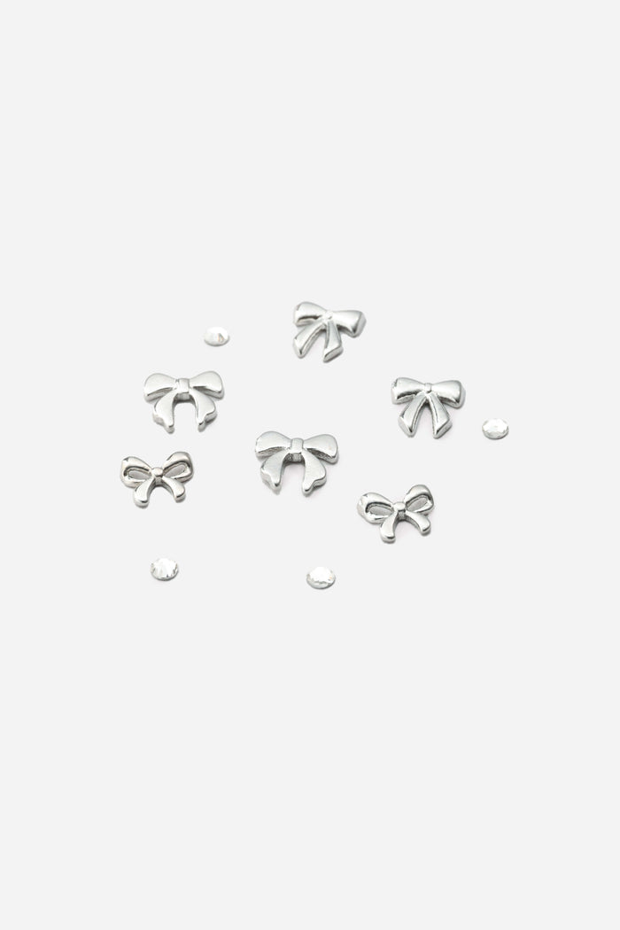 Silver bow-shaped tooth gems with clear crystals scattered on a white background.