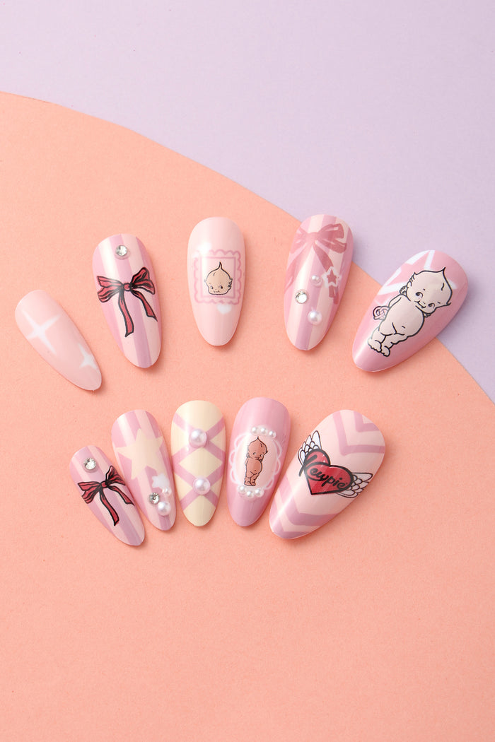 Pink and purple striped press-on nails with bows, pearls, stars, and Kewpie illustrations. Features heart with "Kewpie" and wings.