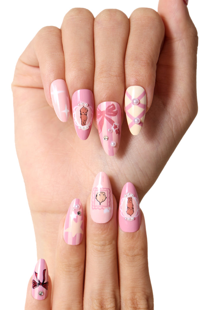 Pink press-on nails featuring Kewpie characters, bows, stars, and pearls.