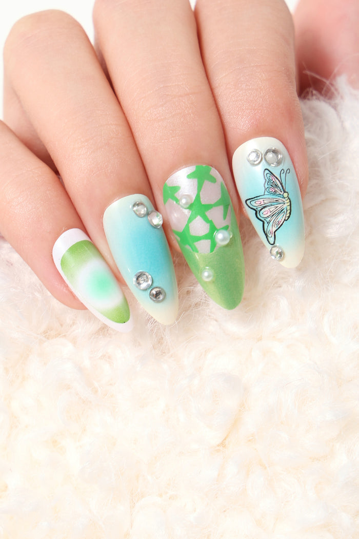 Bratty Kewpie press-on nails with pastel blue, green, and white ombré, featuring a butterfly design and rhinestones.