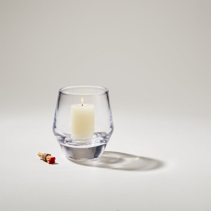 Clear glass votive holder with lit cream-colored candle inside and matches beside it.