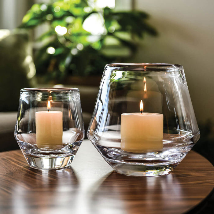 Two clear glass hurricane candle holders with lit cream-colored candles on a wooden surface.