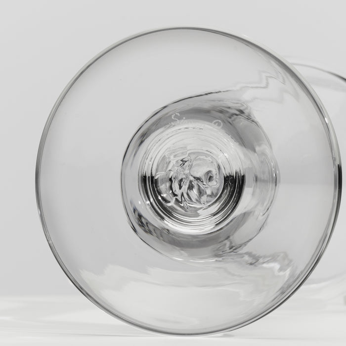 A close-up of a clear glass tumbler, showing the circular base and subtle reflections on a light gray background.