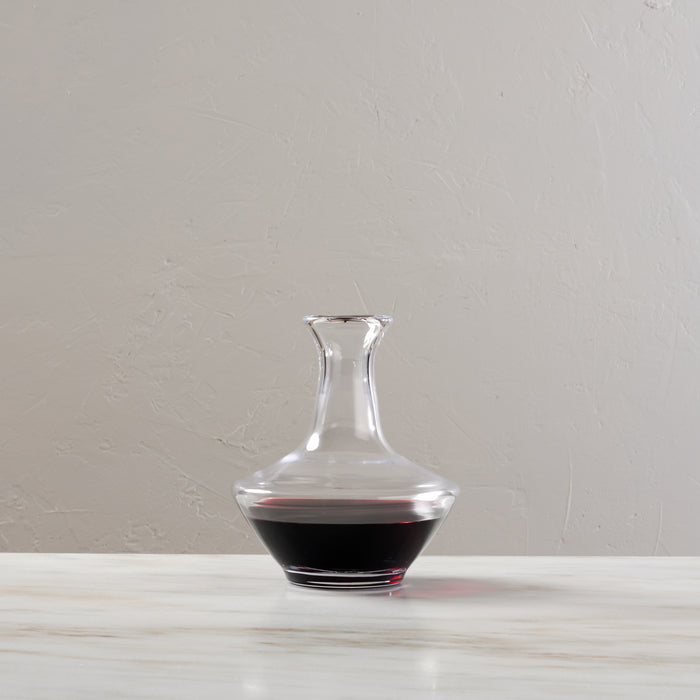 Clear glass wine decanter with wide base and narrow neck, partially filled with red wine.