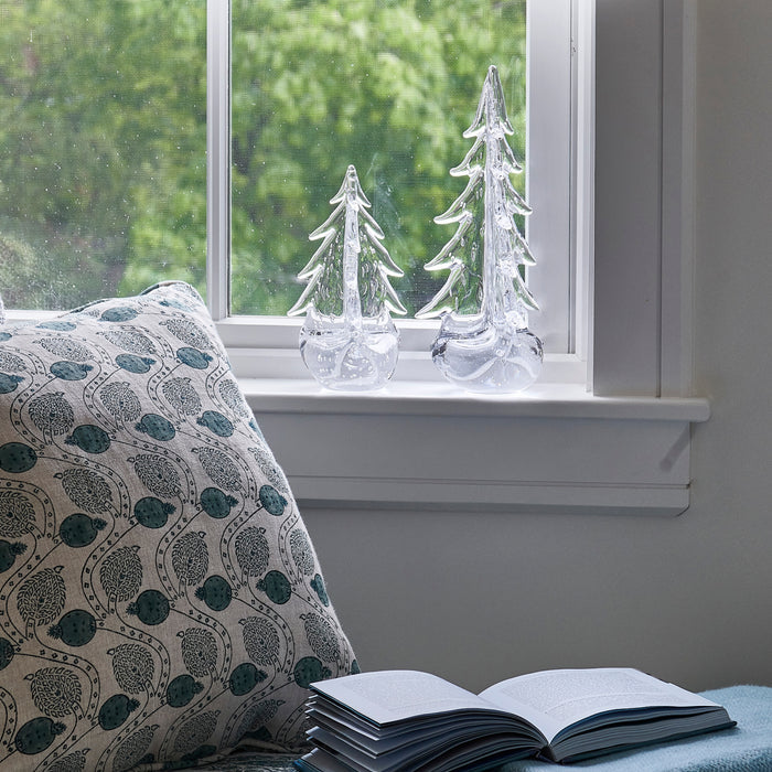 Two clear glass evergreen tree figurines displayed on a white windowsill.