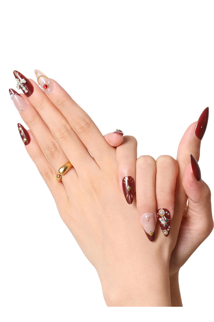 Burgundy French tip press-on nails with intricate gold star designs and pearl accents, featuring a cherub design on one nail.