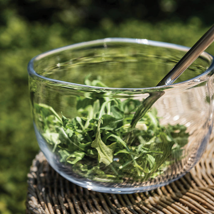 Clear glass bowl filled with green tea and loose leaves, with a spoon resting on the rim.