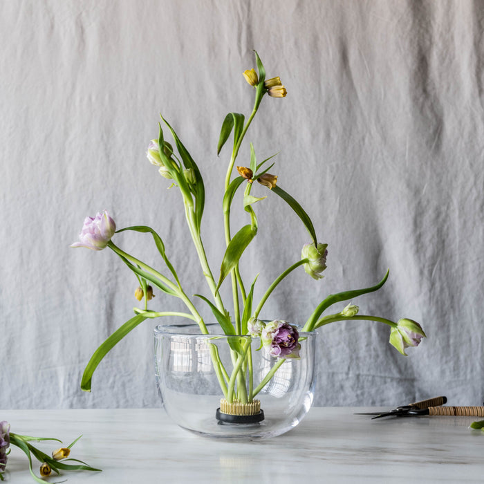 Clear glass bowl with grid pattern containing fresh flowers in various stages of bloom with green stems and leaves.