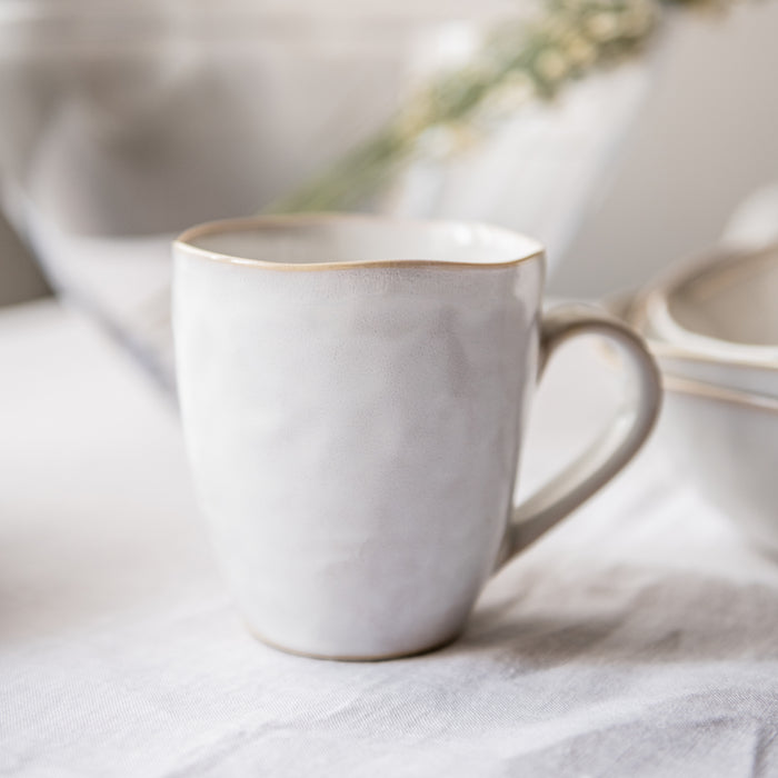 White ceramic mug with tan rim and handle, displayed with matching dinnerware pieces.