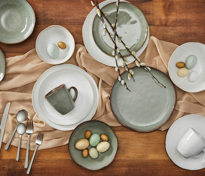 Moss green and white dinnerware set arranged on wooden table with plates, bowls, cups, and flatware.