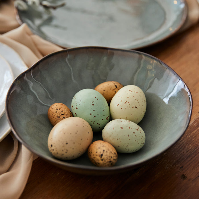 Gray ceramic bowl filled with speckled decorative eggs in brown, cream, and sage green tones.