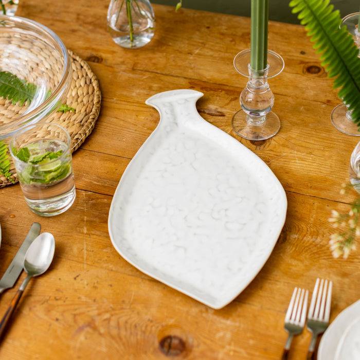White fish-shaped platter with curved tail detail on wooden table setting.