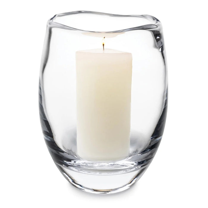 Clear glass hurricane vase with cream-colored pillar candle inside and lit wick.