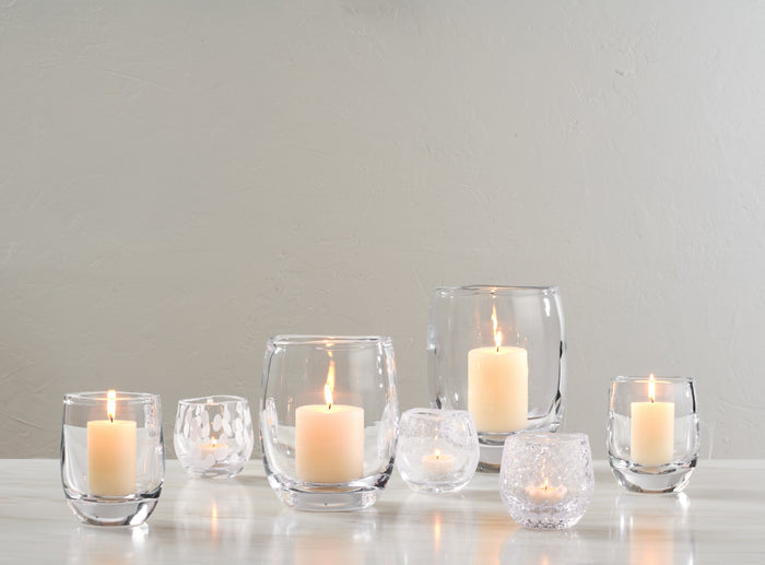 Set of six clear glass hurricane votive candle holders in varying sizes with lit cream-colored candles inside.