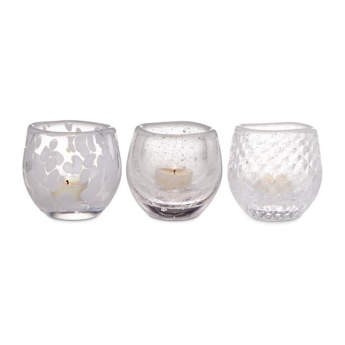 Three frosted glass tealight holders with varied textures containing cream-colored tealight candles.