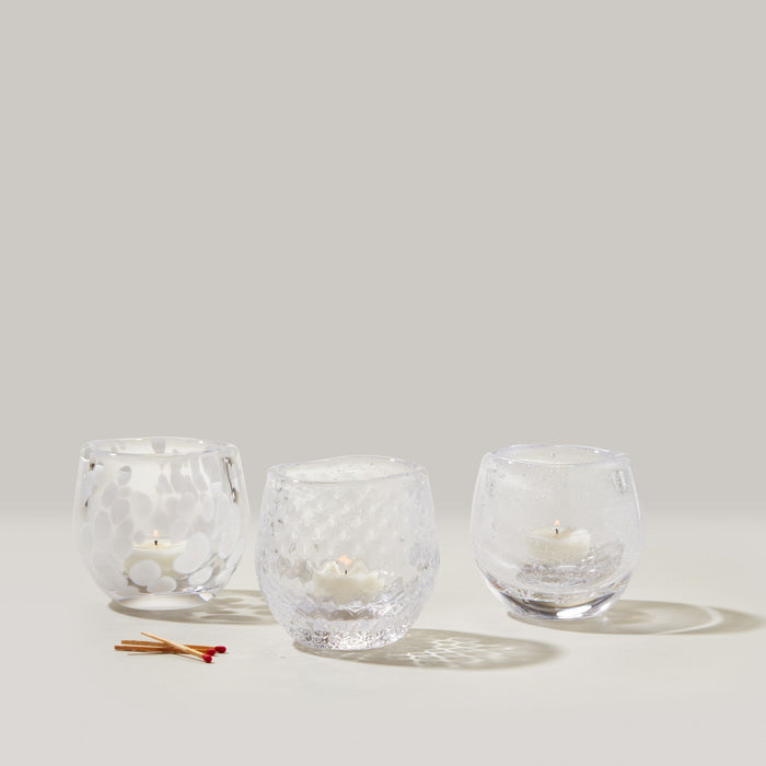 Three clear glass tealight holders with textured surfaces containing white tealight candles, displayed with matches.