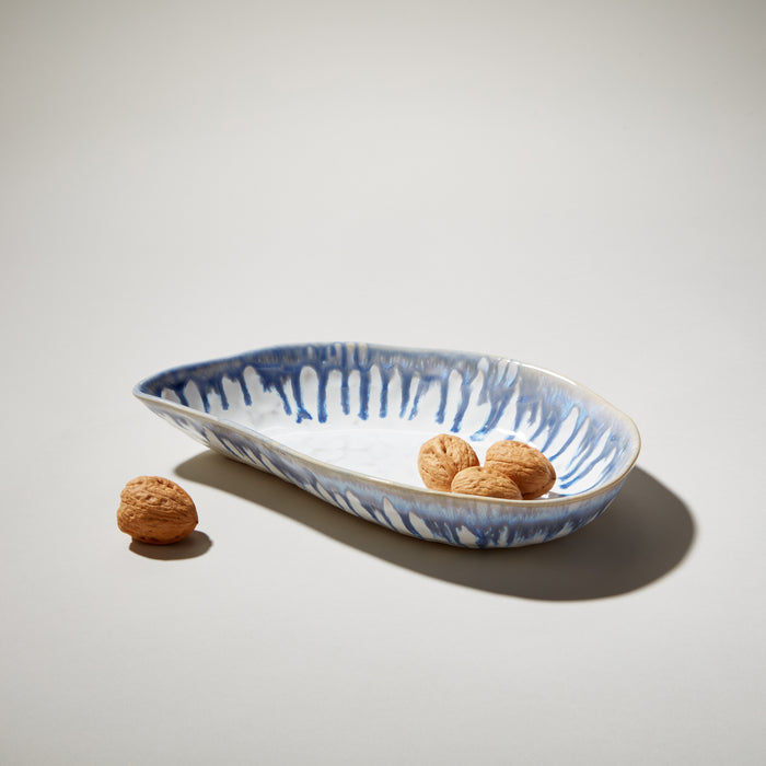 Blue and white ceramic shell-shaped bowl with vertical stripe pattern, containing walnuts.