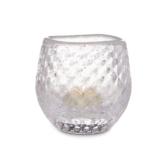 Clear glass tealight holder with textured bubble pattern containing a lit cream-colored candle.