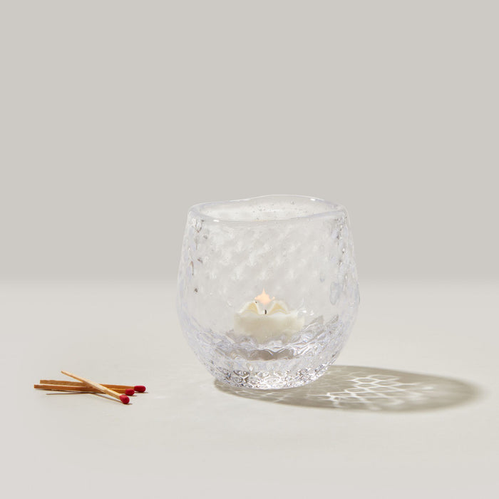 Clear textured glass tealight holder with lit cream candle inside and wooden matches beside it.