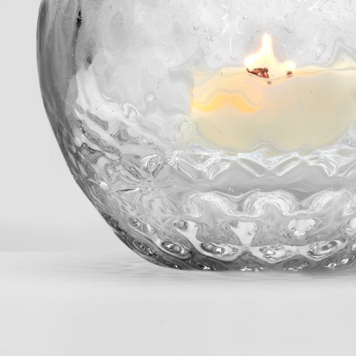 Lit tealight candle inside clear glass bowl with textured, bubble-patterned design.