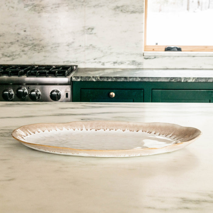 Oval ceramic platter with cream and tan glazed finish and textured rim, displayed on marble countertop.