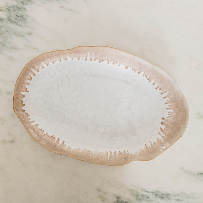 White oval platter with textured tan border and organic wavy edges on marble surface.