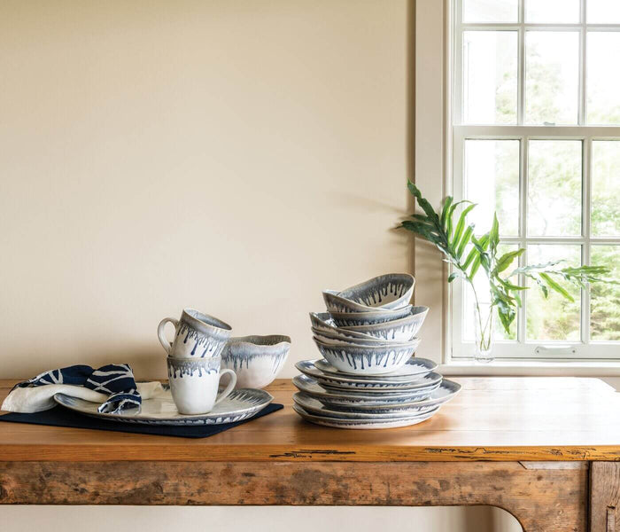 Blue and white ceramic dinnerware set displayed on wooden table with pitcher, bowls, and plates stacked together.