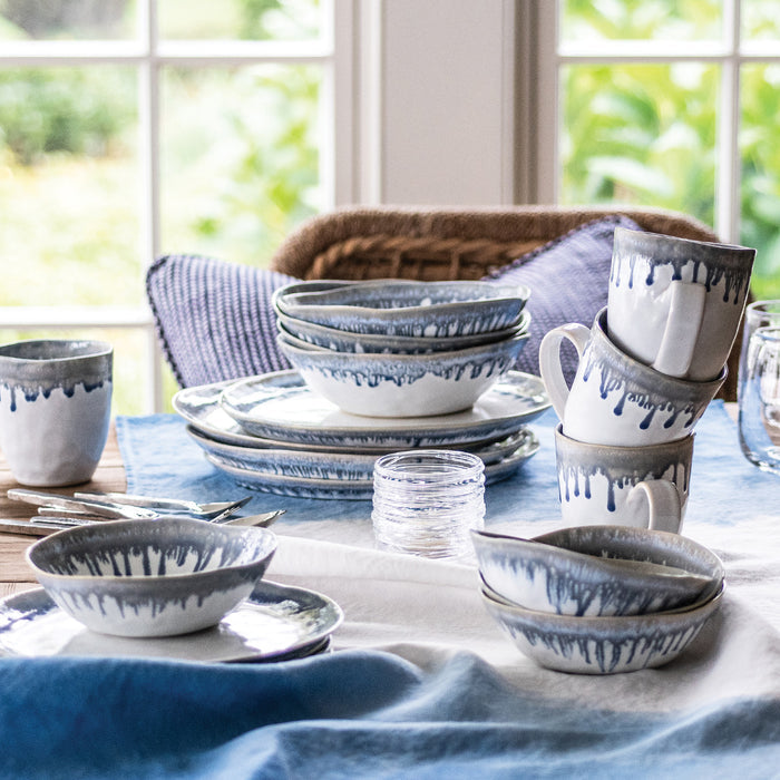 Blue and white dinnerware set with drip-glaze pattern including plates, bowls, and mugs arranged on table.