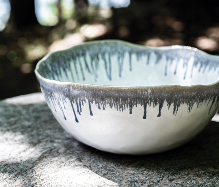 White ceramic bowl with blue drip pattern and wavy rim, shown from above on stone surface.