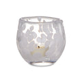 Clear glass tealight holder with frosted snowflake cutout pattern and lit cream-colored tealight candle inside.