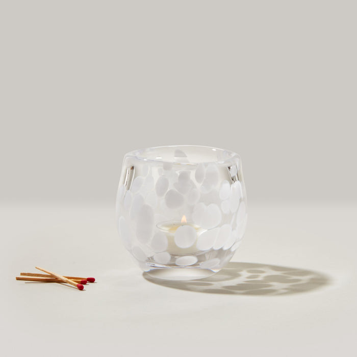 Clear glass tealight holder with white snowflake pattern and lit cream tealight inside, matches displayed next to it.