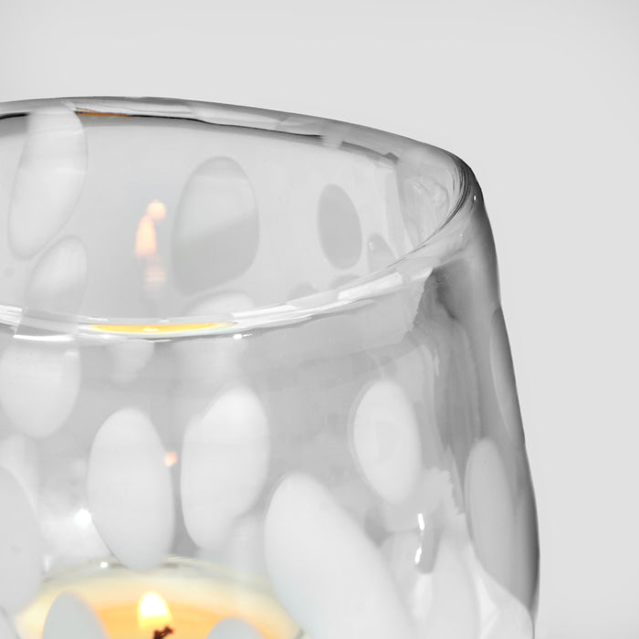 Clear glass holder with white oval pattern containing lit tealight candles with yellow flames.