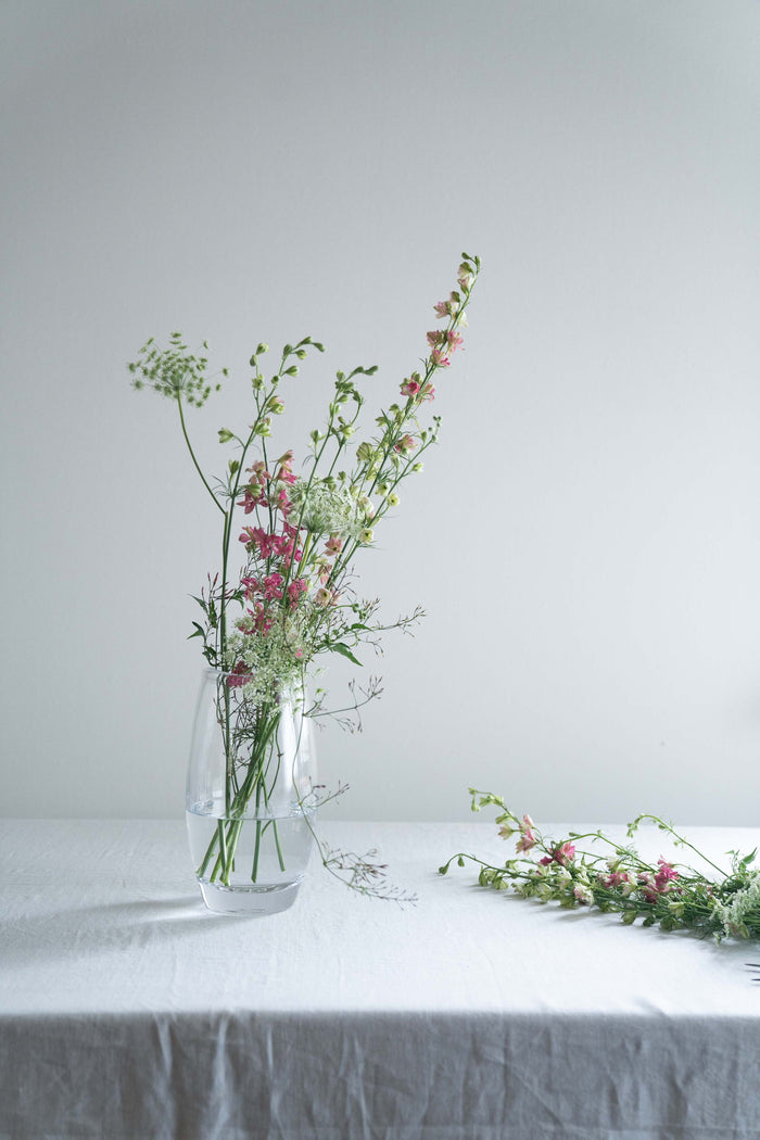 Clear glass vase with mixed dried flowers and greenery arranged inside, including pink blooms and delicate stems.